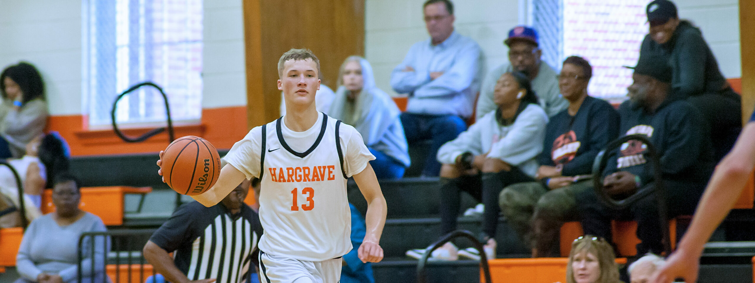 A Hargrave varsity basketball player driving up court in front of a home crowd